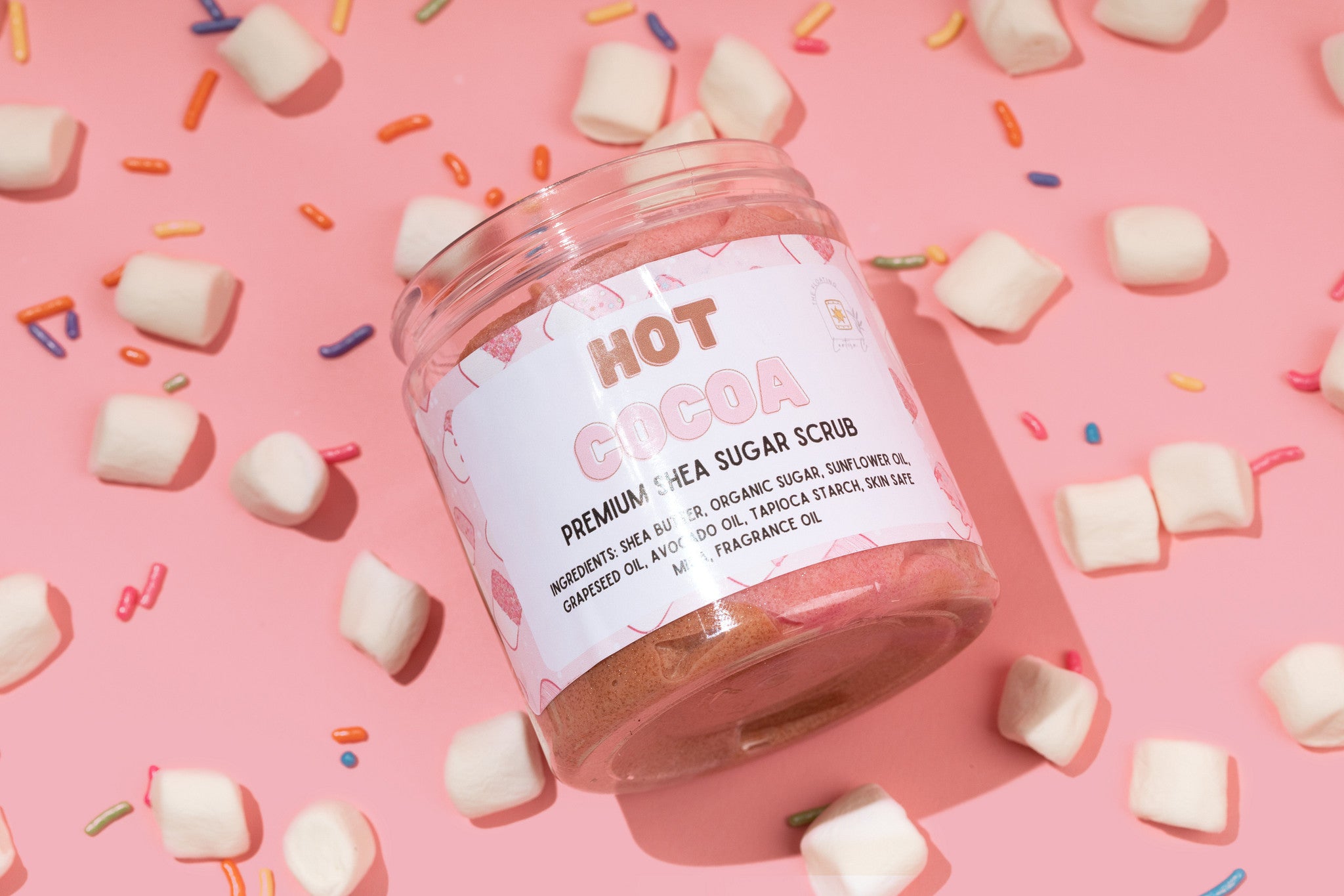 Jar of hot cocoa sugar scrub on a pink background with marshmallows and sprinkles.